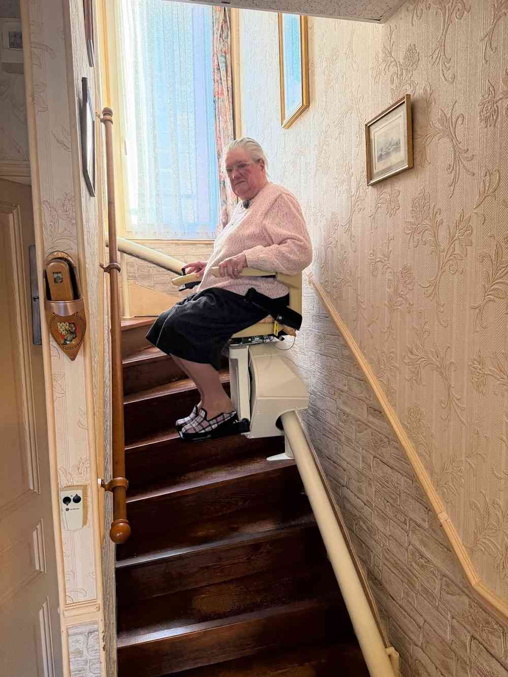 Utilisatrice assise sur son monte-escalier installé à domicile et financé par MaPrimeAdapt'